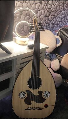 a wooden guitar sitting on top of a table next to a stuffed animal and a laptop computer