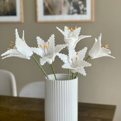 some white flowers are in a vase on a table with two pictures behind it and one is empty