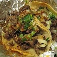 two tacos covered in meat and onions on tin foil