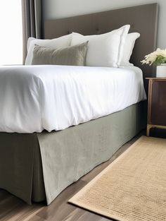 a bed with white sheets and pillows on top of it next to a brown nightstand