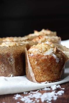 three muffins sitting on top of a wooden table covered in coconut flakes