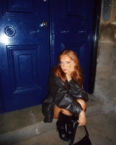 a woman sitting on the ground holding a black purse in front of a blue door