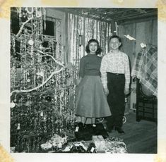 an old black and white photo of two people standing in front of a christmas tree