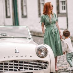 a woman holding the hand of a little boy in front of an old car