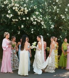 a group of women standing next to each other in front of trees and white flowers