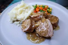 a white plate topped with meat and potatoes covered in gravy next to veggies