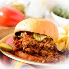 a sloppy joe sandwich with pickles and chips on a plate next to some tomatoes