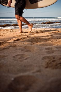 a man carrying a surfboard on top of a sandy beach