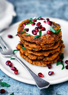 a stack of pancakes topped with pomegranates on a plate next to a fork