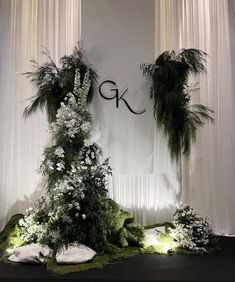 an arrangement of flowers and greenery on display in front of curtains