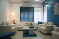 a living room filled with white furniture and blue accent wall covering the window sill