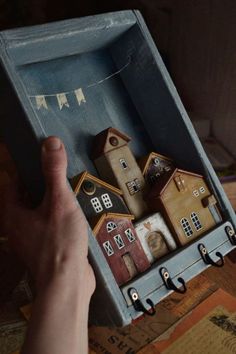 a hand is holding an open box with miniature houses in it