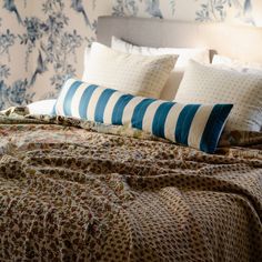 an unmade bed with blue and white floral wallpaper