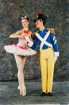 a man and woman dressed in costumes standing next to each other, one holding a heart