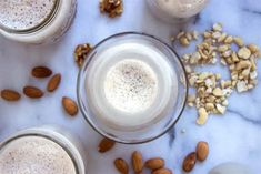 three glasses filled with milk and nuts on top of a marble countertop next to some almonds