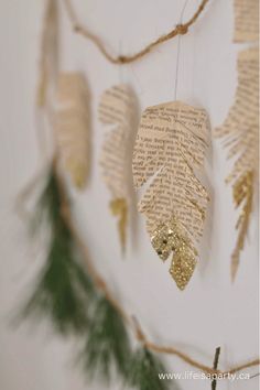 some paper leaves are hanging from a string with gold glitters on them and there is a pine branch in the foreground