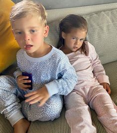 two young children sitting on a couch with remote controls