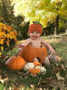 a baby sitting in a pumpkin costume surrounded by fall leaves and gourds, smiling at the camera