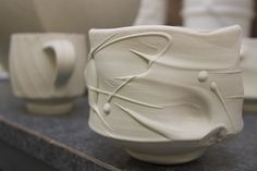 two white cups sitting next to each other on top of a counter with one cup in the shape of a cat's head