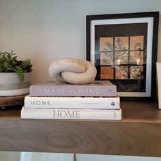 three books stacked on top of each other next to a candle and potted plant