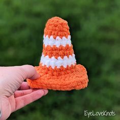 an orange and white crocheted hat is held up by someone's hand