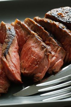 some meat is sitting on a plate with a fork and knife next to the steak