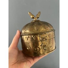 a hand holding an ornately decorated brass box