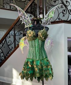 a green corset with wings and flowers on display in front of a stair case