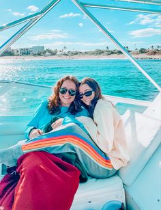 two women are sitting on the back of a boat in the water, wrapped up