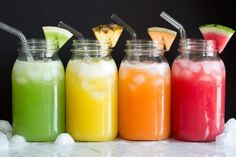 four different colored drinks lined up in mason jars with straws and watermelon