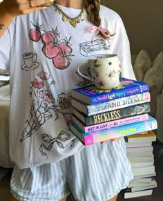 a woman holding a stack of books and a coffee mug in her hand while wearing pajamas