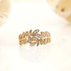 a gold ring with leaves and diamonds on the side, sitting next to flowers in front of it