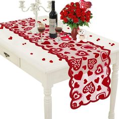 a white table topped with a vase filled with red flowers next to a bottle of wine