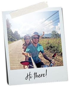 a man and woman riding on the back of a motor scooter down a dirt road