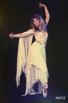 a woman dressed in white is dancing with her arms spread out and hands extended to the side