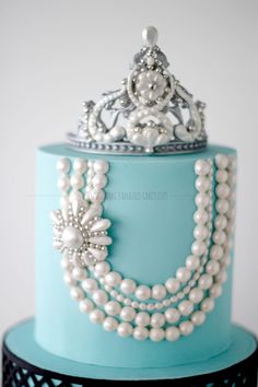 a cake with pearls and a tiara on top is decorated in blue icing