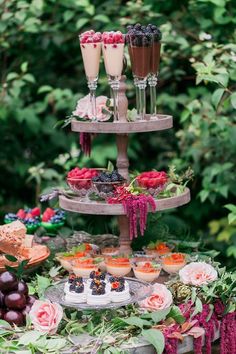 an assortment of desserts are displayed on a table in the garden with flowers and greenery