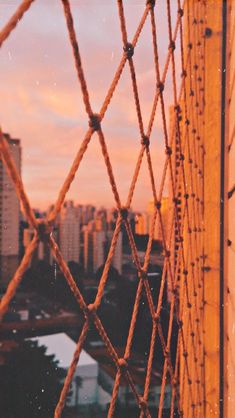 an orange and pink sky behind a chain link fence with the city in the background