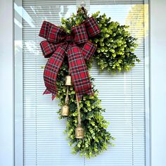 a wreath with bells hanging on the side of a door that is decorated with greenery