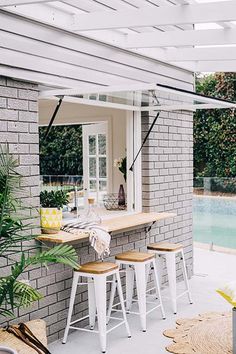 an outdoor bar with stools next to a swimming pool in a house that's built into the side of a brick wall