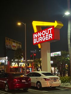 two cars are parked in front of a fast food restaurant at night with neon lights