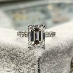 an emerald - cut diamond ring sits on a fur covered surface