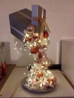 a small christmas tree with lights and ornaments on it's base in front of a gift box