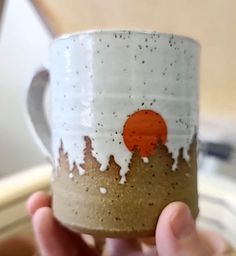 a hand holding a coffee cup with white and orange paint splattered on it