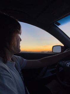 a woman driving a car with the sun setting in the background