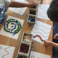 two children working on crafts at a table with paper cut outs and beads in boxes