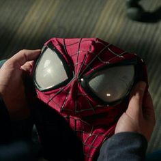 a spider man mask is being held by someone's hands in front of him