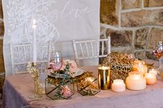 a table with candles, wine glasses and other items on it in front of a stone wall