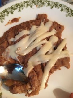 a white plate topped with meat covered in sauce and gravy next to a spoon