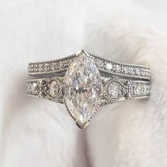 an engagement ring with a pear shaped diamond surrounded by smaller round diamonds on a white fur background